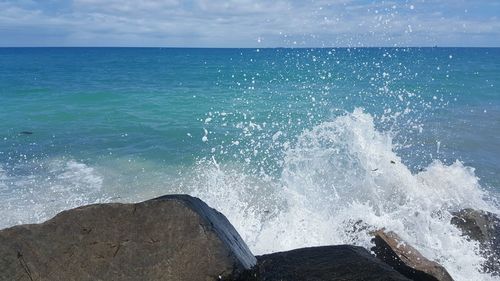 Waves splashing on shore against blue sky