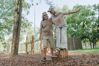 Senior man supporting woman balancing on tree stump in park