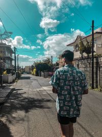 Rear view of man walking on street against sky