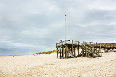 Low angle view of pier on sandy beach against cloudy sky