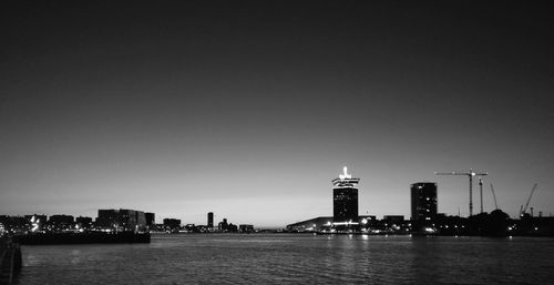 River by illuminated buildings against clear sky at night