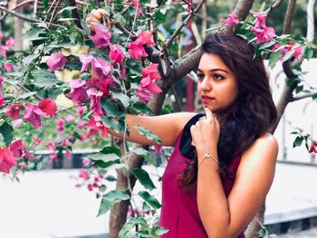 Young woman looking away while standing by flowering plant