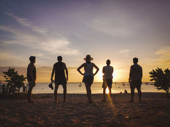 Rear view of people on beach against sky during sunset