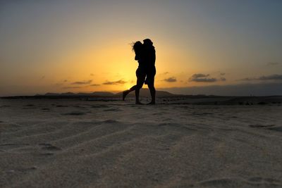 Silhouette couple standing on sand dune against sky during sunset