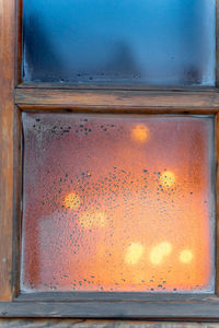Close-up of wet glass window against sky