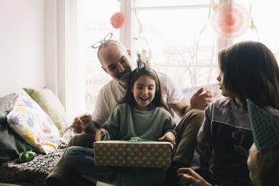 Surprised girl holding birthday present while sitting with brother and father at home