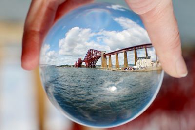 Cropped hand holding crystal ball against sea