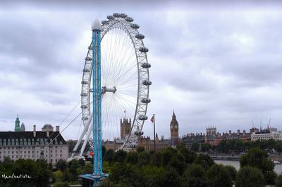 Ferris wheel in city against cloudy sky