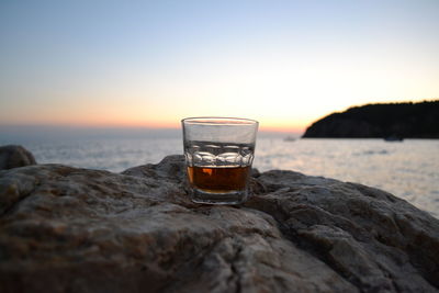 Whiskey glass on rock against sea during sunset