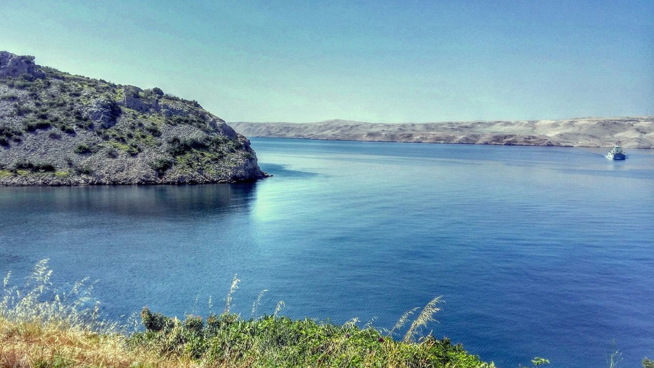 water, tranquil scene, tranquility, sea, scenics, beauty in nature, blue, mountain, nature, clear sky, sky, idyllic, horizon over water, plant, cliff, copy space, lake, day, remote, rock - object