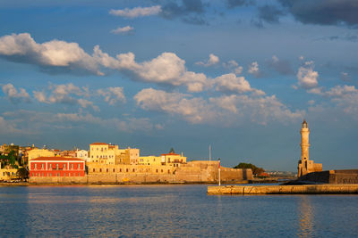 Buildings at waterfront against cloudy sky