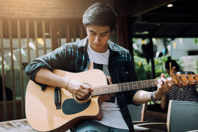 Young man playing guitar while sitting on table at outdoor restaurant