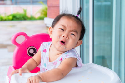 Cute baby girl crying while sitting on high chair