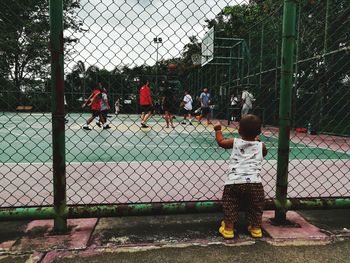 Rear view of a boy playing with chainlink fence