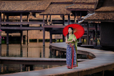 Smiling young woman standing with umbrella on pier against stilt houses