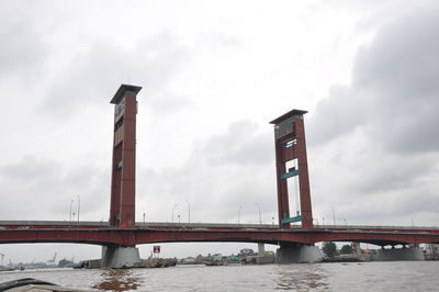 Low angle view of bridge over river against cloudy sky