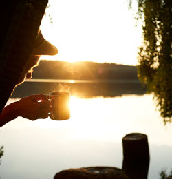 Close-up of hand holding drink against sky during sunset