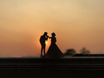 Silhouette man kissing on woman hand against sky during sunset