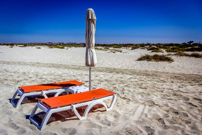 Orange lounge chairs at beach against clear sky