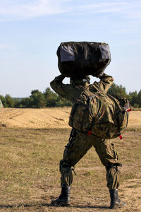 Army soldier with bags walking on field against sky