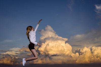 Side view of young woman jumping against cloudy sky