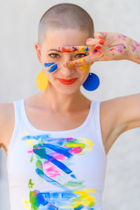 Gorgeous female artist painter covered in paint, looking and smiling at camera through her fingers. 