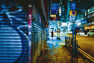 People walking on illuminated street amidst buildings at night