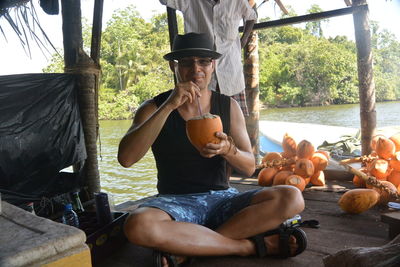 Portrait of man drinking coconut water while sitting on boat in river