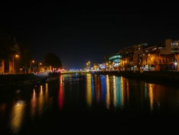 Illuminated city by river against sky at night