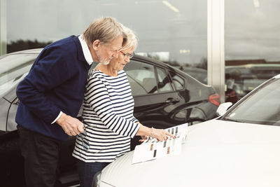 Senior couple looking at brochure on car outside showroom