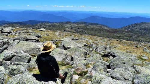 Rear view of man sitting on top of mount  kosciuszko looking at mountains