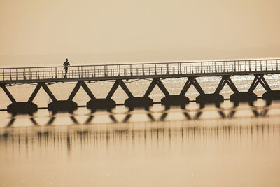 Person on bridge over sea against clear sky during sunset