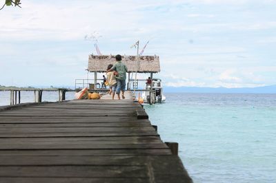 Rear view of brothers running on pier over sea against sky