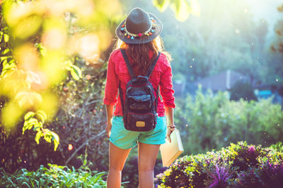 Rear view of woman wearing hat holding book while standing at park