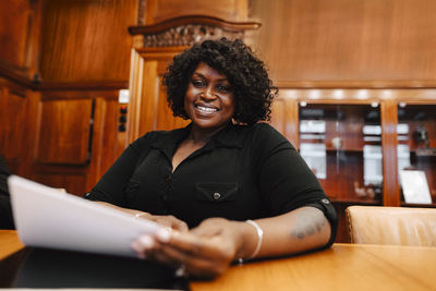 Portrait of smiling businesswoman holding contract document sitting at conference table in board room during meeting