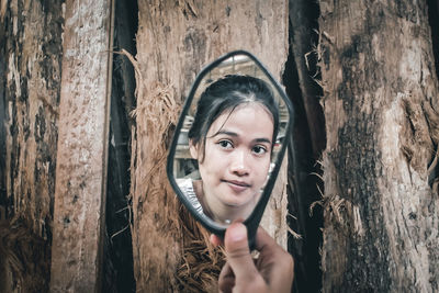 Portrait of a smiling young woman against tree trunk