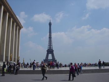 People walking on city square in front of eiffel tower against sky