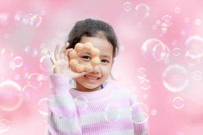 Portrait of smiling girl playing with bubbles against pink background