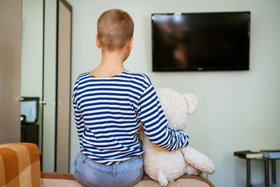 Cute boy and his plush toy bear are watching tv while sitting on the couch