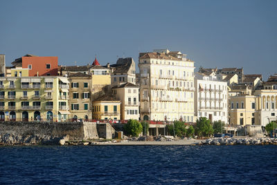 Buildings by sea against clear blue sky