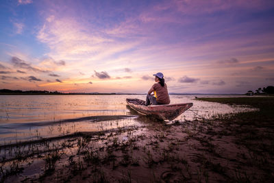 Man on boat at beach against sky during sunset