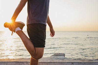 Man stretching his leg at sunrise near the sea with the sun in the background and lens flare.