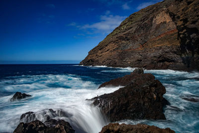 Scenic view of rocks on beach against blue sky