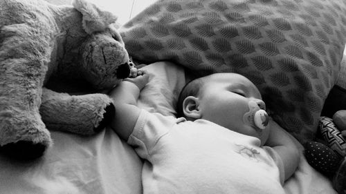 High angle view of baby with pacifier in mouth sleeping on bed at home