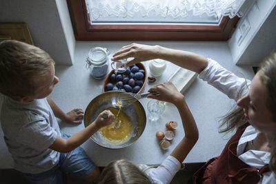 Woman cooking cake of plums with children at home