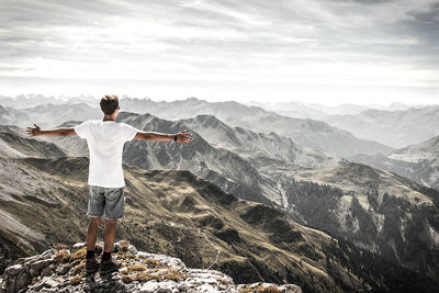 Rear view of man with arms outstretched on top of a mountain in the alps