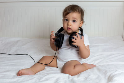 Baby boy in big headphones in white big bed