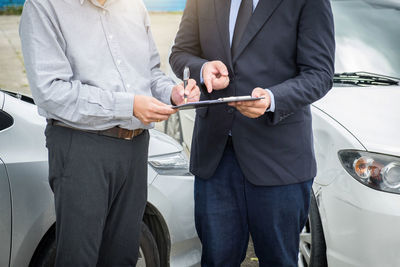 Midsection of businessman signing document with male coworker against cars