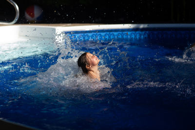 Girl splashing water while swimming in pool