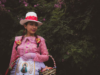 Smiling young woman standing against plants